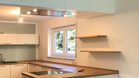 Offene Küche mit geöffneter Wand zum Wohnraum, integrierter Decken‑Ablufthaube und Architekturbeleuchtung